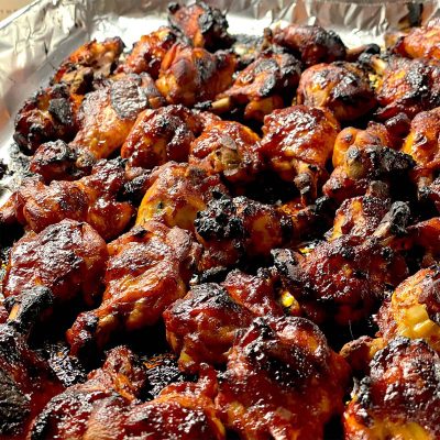Barbecue chicken wings covered in a glossy, caramelised sauce, slightly charred, arranged closely together on a foil-lined baking tray.