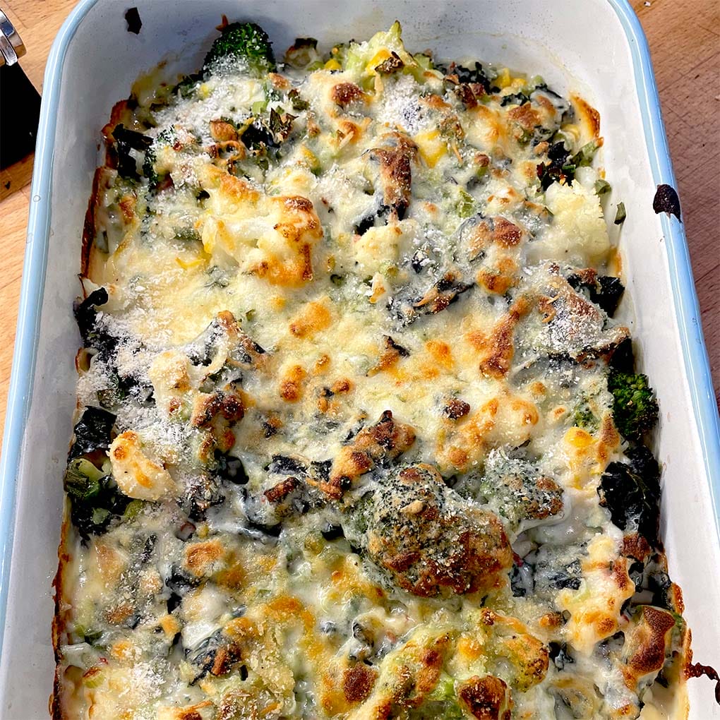 A baked casserole dish filled with broccoli, cauliflower, and melted cheese, browned on top, sitting on a wooden surface.