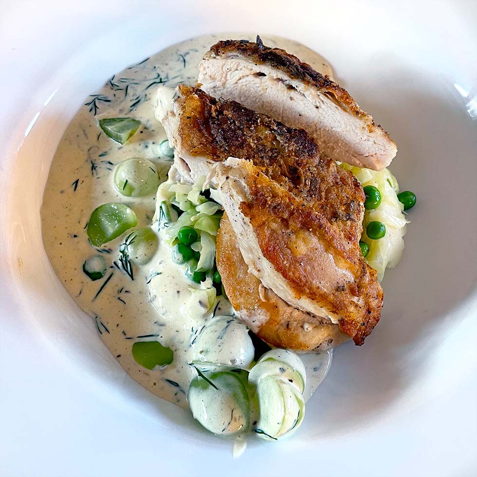 Sliced roasted chicken breast served over creamy pasta with garden peas and courgette, garnished with fresh herbs in a white bowl.