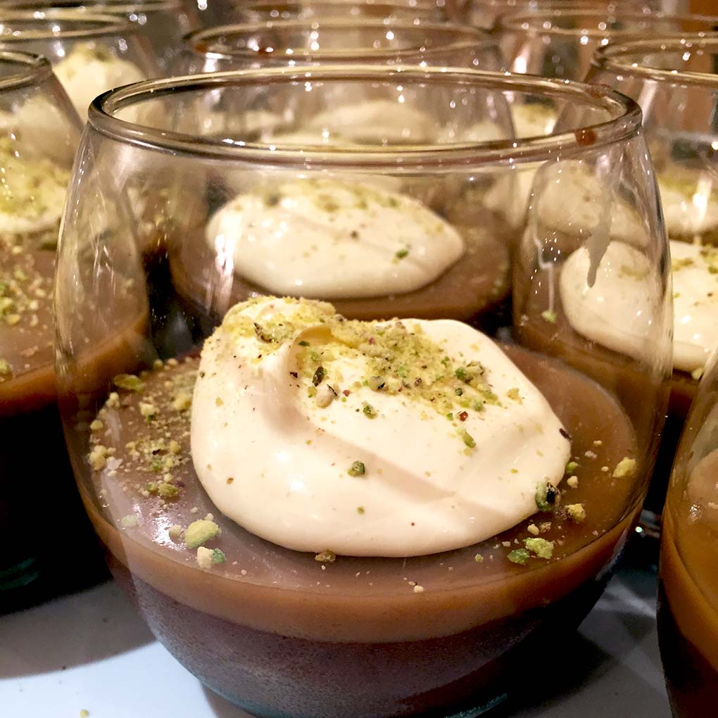 Glasses filled with chocolate mousse, each topped with a dollop of whipped cream and sprinkled with crushed pistachios.