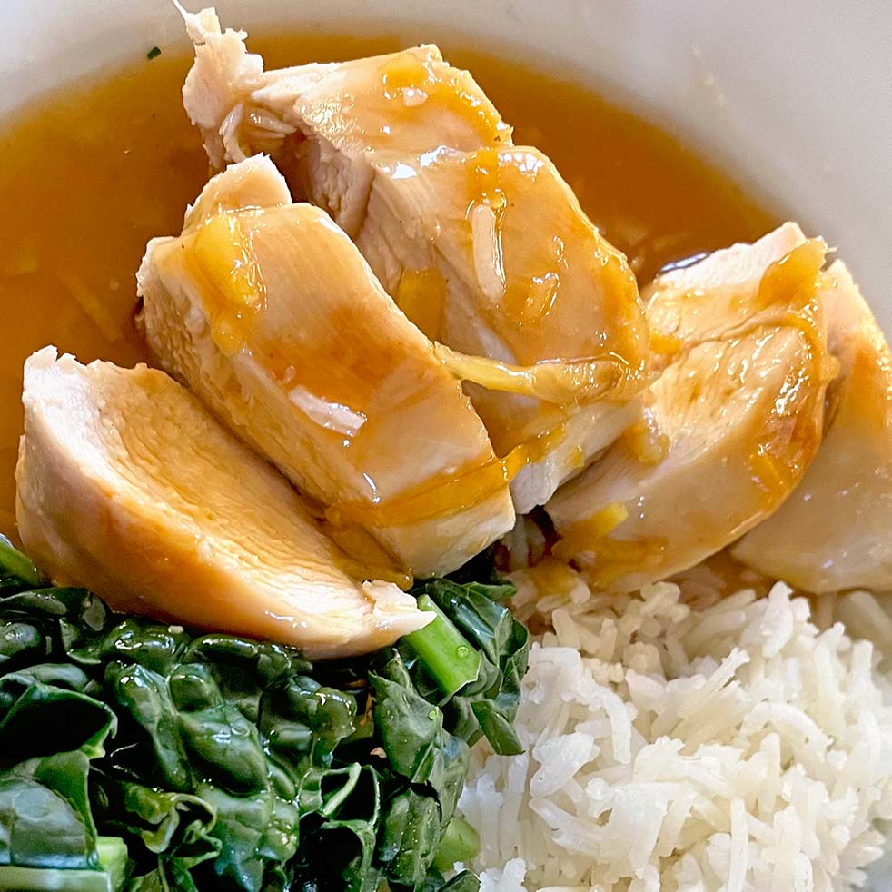 Sliced chicken breast drizzled with brown sauce, served with steamed white rice and leafy cooked greens on a white plate.