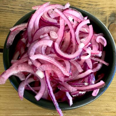 A black bowl filled with thinly sliced red onions, placed on a wooden surface.