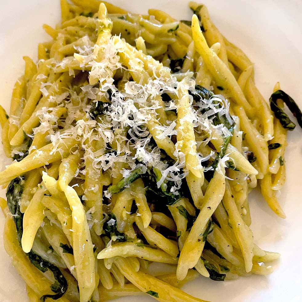 A plate of pasta topped with grated cheese and mixed with green leafy vegetables, served on a white plate.
