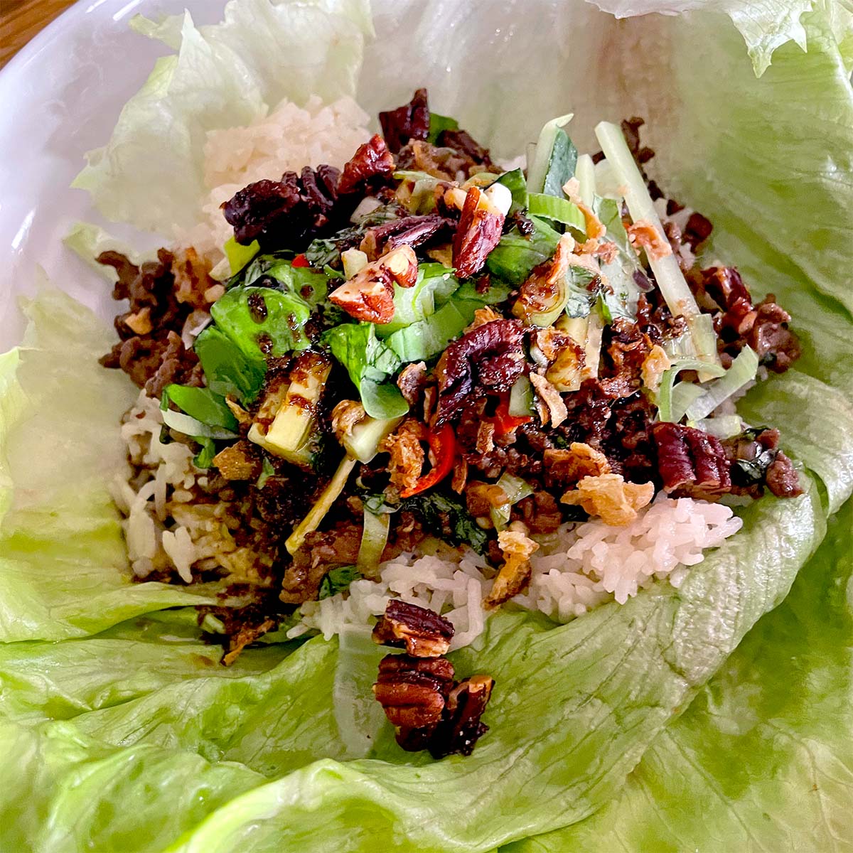 A lettuce leaf filled with white rice, minced meat, chopped spring onions, pecans, and assorted vegetables, served as a wrap.