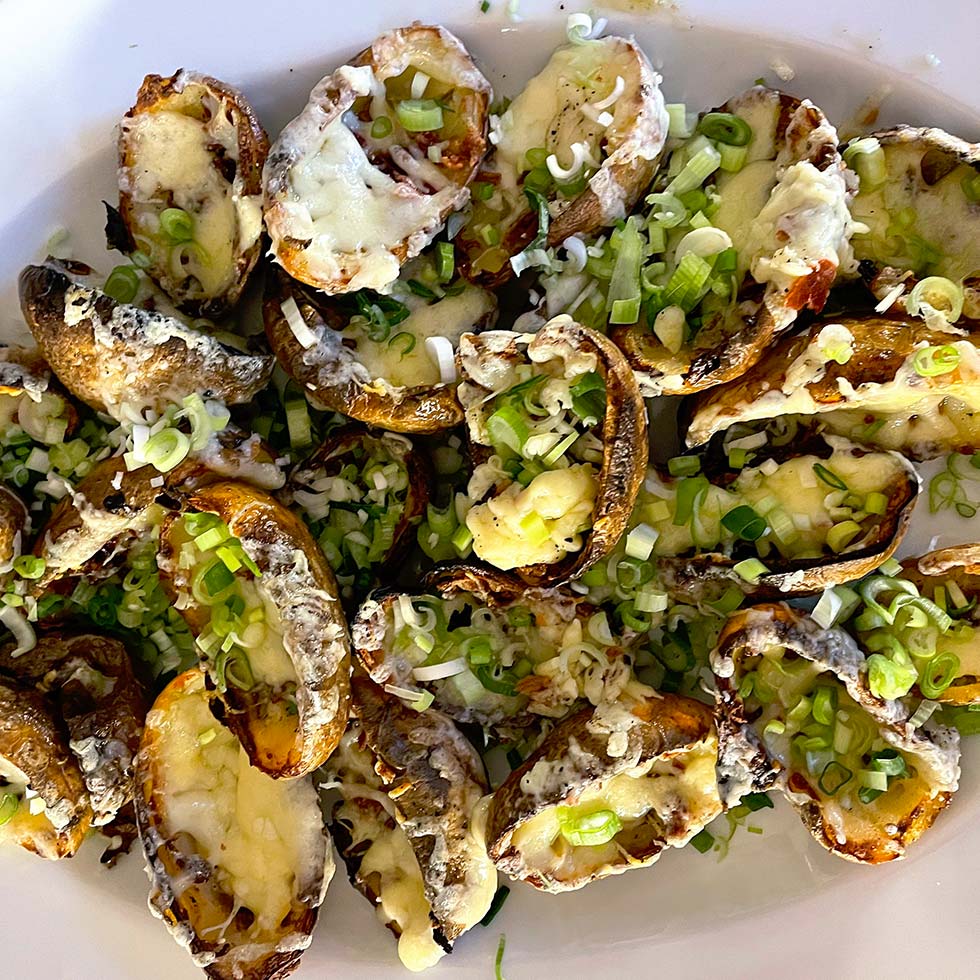 A plate of baked potato skins topped with melted cheese and chopped spring onions, arranged closely together on a white dish.