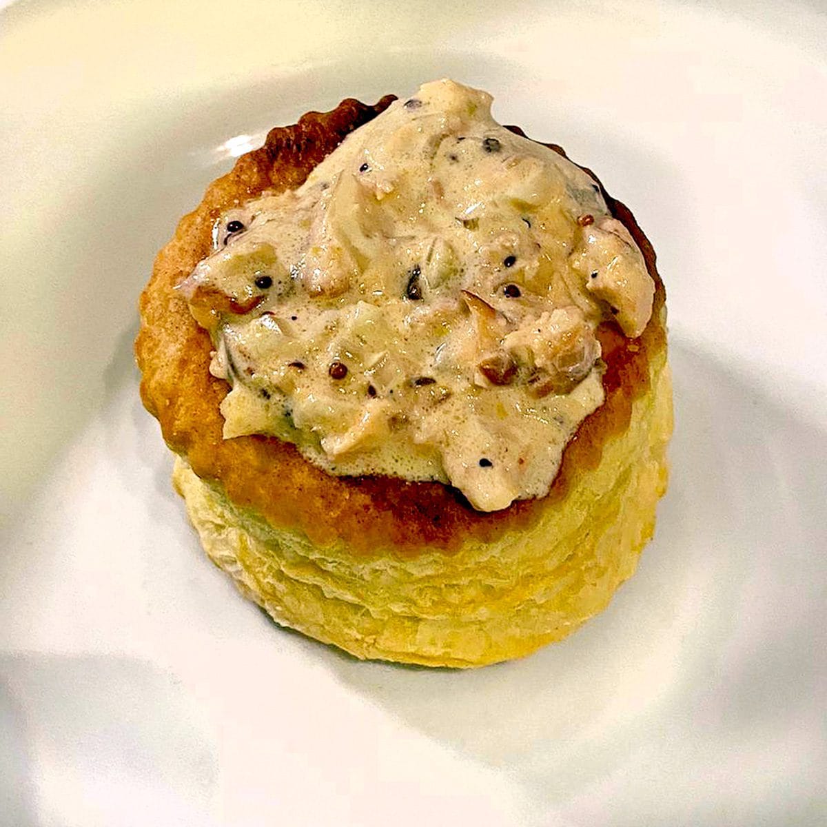 A golden, round puff pastry case filled with a creamy, mushroom and herb sauce, served on a white plate.